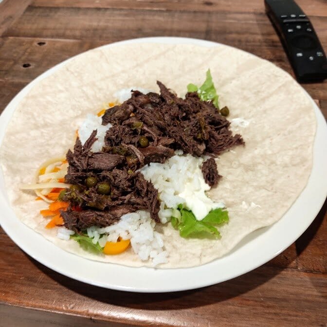 Some pulled duck sitting in a wrap with rice and salad. 