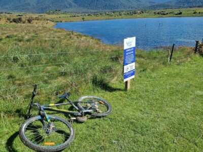 Wider viewer of the top of Loch Katrine My bike in the foreground with a Fish and Game Angler Access information board and Loch Katrine in the background