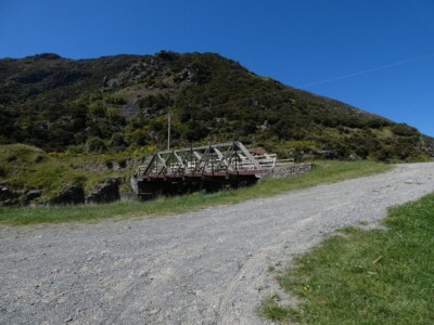 Another view of the historic bridge, from where I was parked to air down my tyres. The historic bridge back from where I was parked. With a gravel entranceway in front and bushy hills in the back.